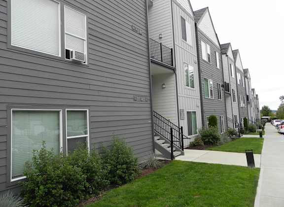A row of grey townhouses with green lawns in front.