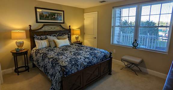 A bedroom with a large bed and a window overlooking a fence.