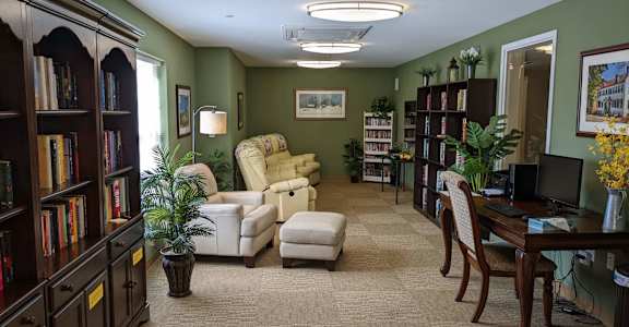 A room with a carpeted floor, a desk, a chair, and a bookshelf.