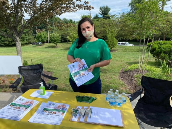 a woman wearing a mask stands behind a table with supplies