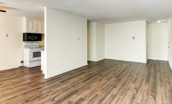 an empty living room with a kitchen in the background