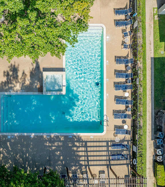 A swimming pool surrounded by trees and chairs.