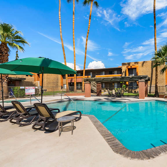 A pool surrounded by palm trees and lounge chairs.