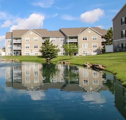 This is a picture of a fountain in a pond with building exteriors at Nantucket Apartments, in Loveland, OH.