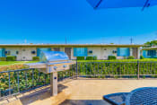 Thumbnail 20 of 25 - Apartments in Colton, CA - Enclosed Picnic Area Featuring Grill and Covered Tables with Bench Seating, Surrounded by Lush Landscaping and Las Brisas Apartment Buildings