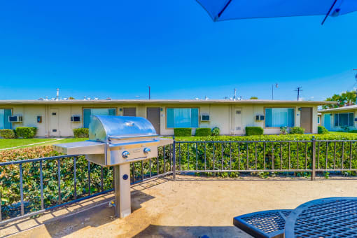 Apartments in Colton, CA - Enclosed Picnic Area Featuring Grill and Covered Tables with Bench Seating, Surrounded by Lush Landscaping and Las Brisas Apartment Buildings