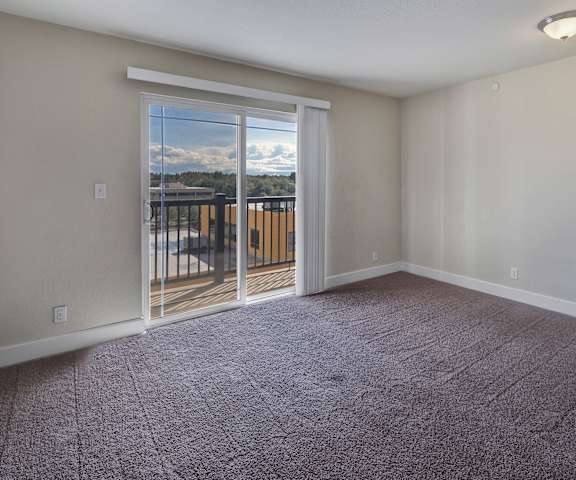 An empty living room with carpeting and a door to the balcony at City View Apartments. 