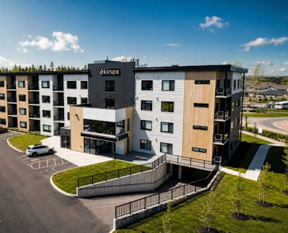 A modern apartment complex named "aknox" is surrounded by a parking lot and greenery.