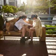 Two women sitting on a bench in a sunny outdoor setting.