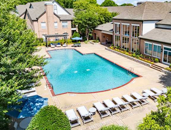 A large swimming pool surrounded by lawn chairs and trees.