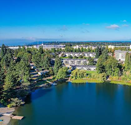 A serene lake surrounded by lush greenery and buildings in the distance under a clear blue sky.