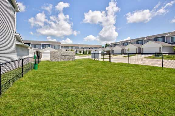 A grassy area in front of a row of houses with a fence and a green trash can.