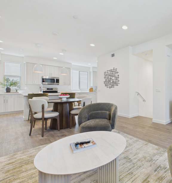 A modern living room with a beige couch, a coffee table, and a kitchen area in the background.
