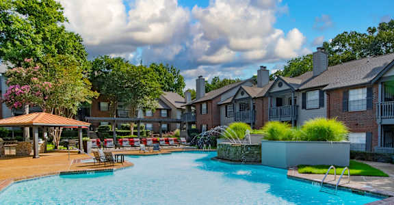 A large swimming pool surrounded by a brick border and a grassy area with a bench.