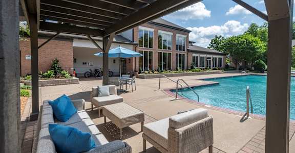 A patio with a couch and chairs under a roof next to a pool.