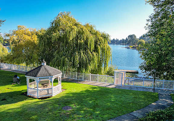 A gazebo sits in a grassy area next to a lake.