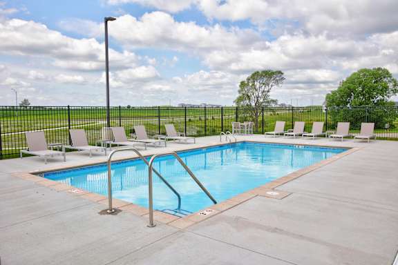 A pool with a metal ladder and white chairs.