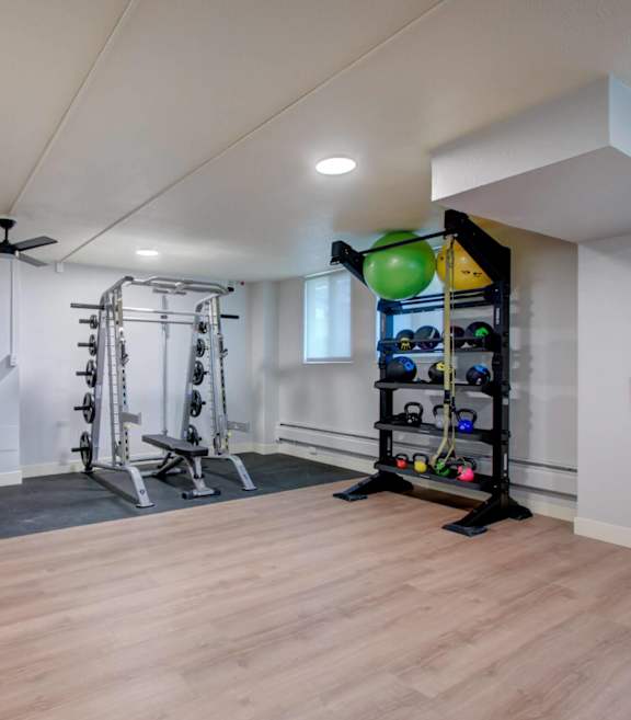 A gym room with a variety of equipment including a squat rack, bench, and a wall-mounted rack with multiple resistance bands.