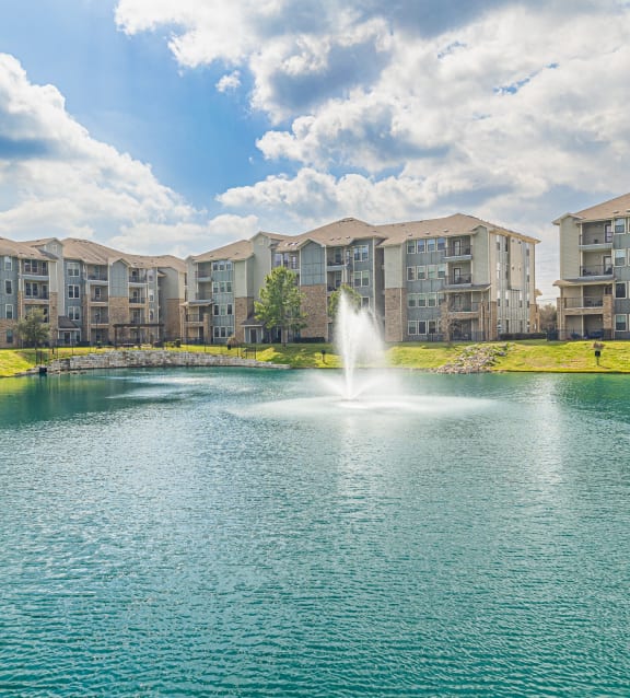 a pond with a fountain in front of an apartment building
