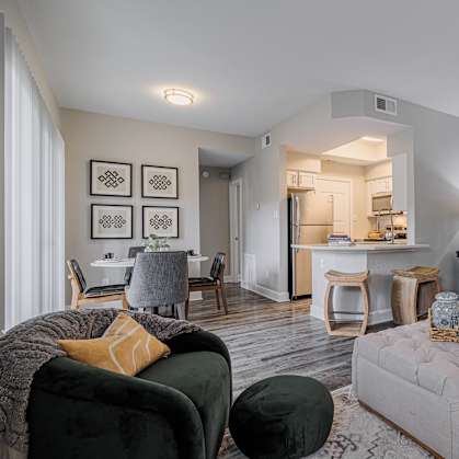 a living room with a couch and a ottoman in front of a kitchen