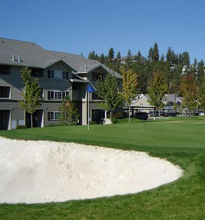 A golf course with a sand trap in the foreground and houses in the background.