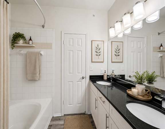 A bathroom with a white door, a white tub, and a black counter.