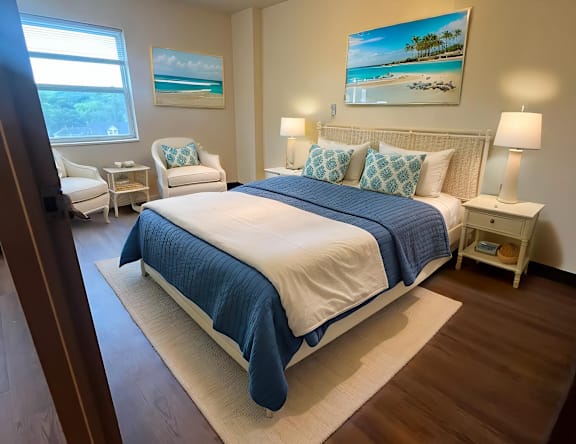 A bedroom with a bed, two chairs, and a painting on the wall.