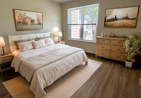 A bedroom with a large bed, a dresser, and two paintings on the wall.