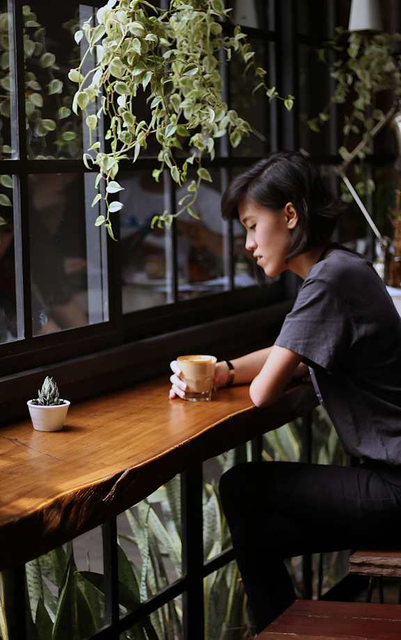 A woman sitting at a table with a plant in a pot and a stack of books.