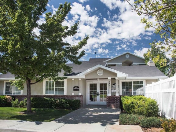 the front of a house with a tree and a white fence  at Country Oaks Apartments in Clearfield, Utah