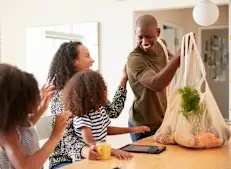 A man is showing a bag of groceries to a group of people around a table.