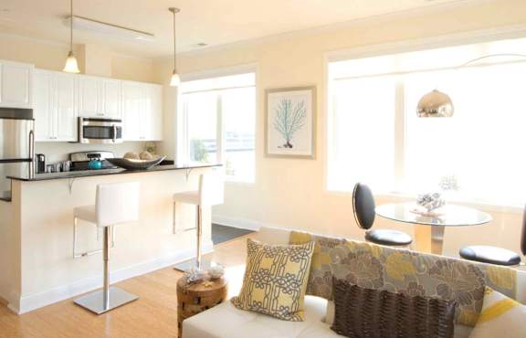 A modern kitchen with a white countertop and a white couch with yellow and brown pillows.