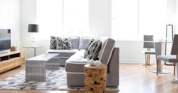 A modern living room with a grey sofa, a glass table, and a wooden coffee table.