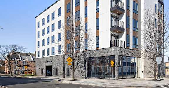 A modern multi-story building with a white and brown facade and balconies on the upper floors.