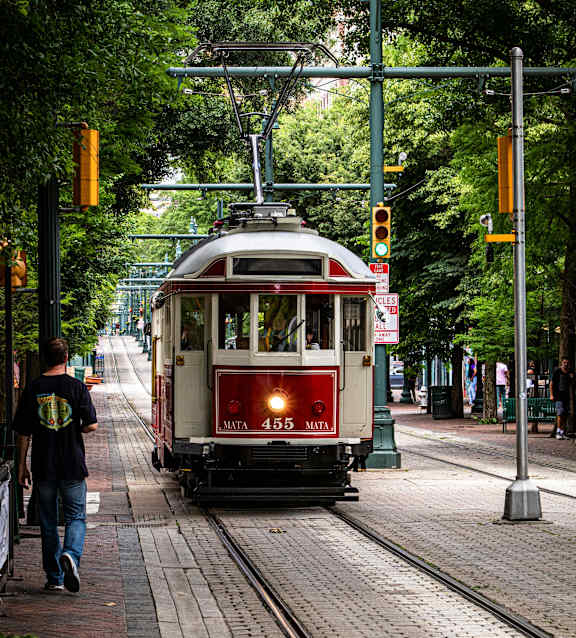 A red and white tram with the number 455 on it is on a track in the middle of a street.