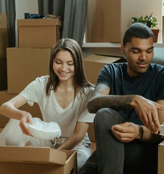 A man and woman are sitting on the floor surrounded by moving boxes.