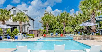 A pool with white chairs and a house in the background.