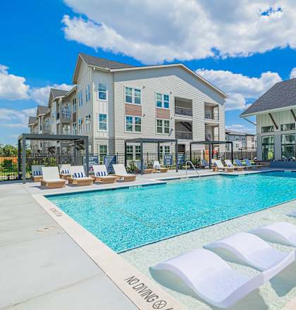 A pool with lounge chairs and a building in the background.
