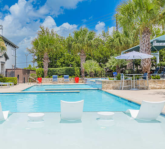 A pool with white chairs and a house in the background.