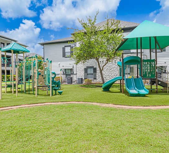 A playground with a green slide and a green umbrella.