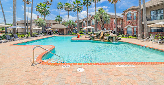 A pool surrounded by palm trees and a red brick building.
