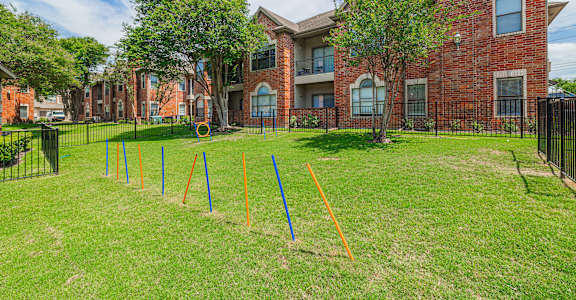 A grassy area in front of a brick building with orange and blue poles sticking out of the ground.