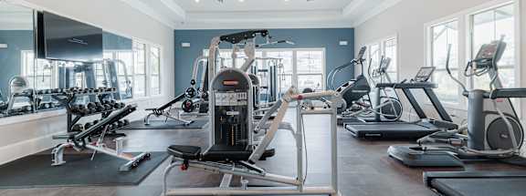 A gym with a variety of exercise equipment including treadmills, elliptical machines, and a weight machine.