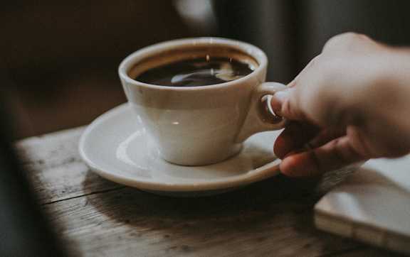 A person is holding a cup of coffee on a saucer.
