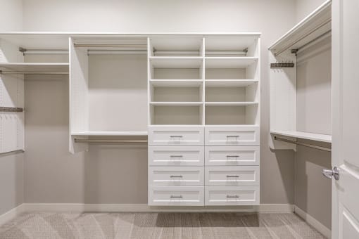 a walk in closet with white shelves and drawers