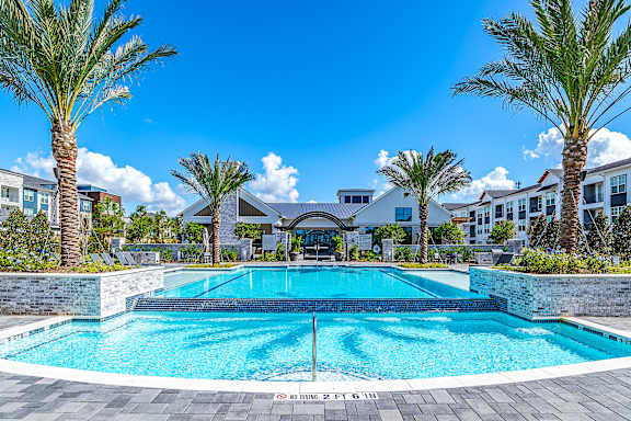  A swimming pool surrounded by palm trees and a building in the background.