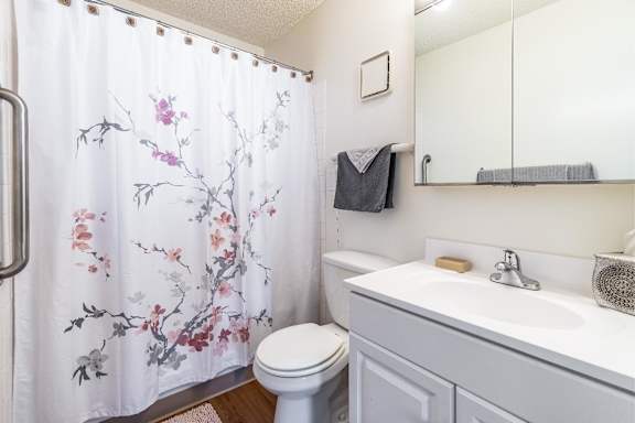 A white bathroom with a floral shower curtain and a toilet.