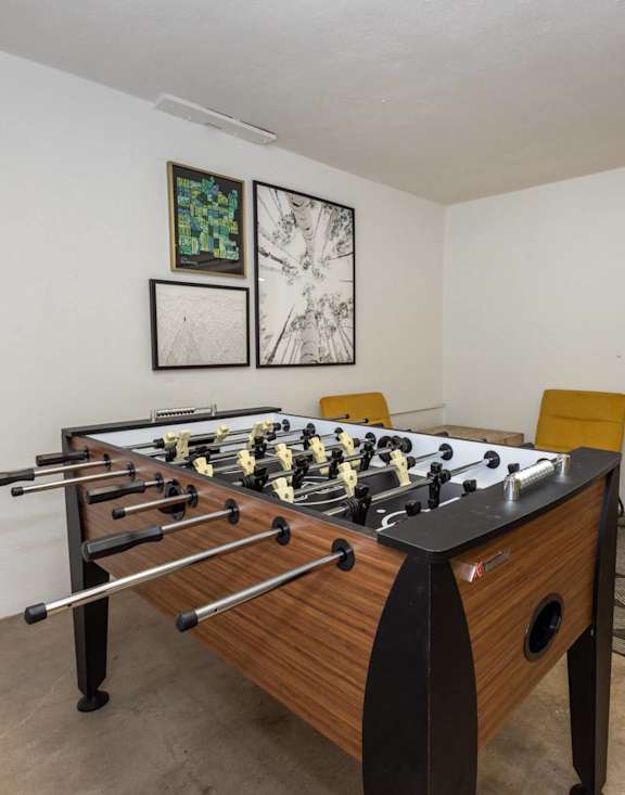 A foosball table sits in a room with a rug and two framed pictures on the wall.