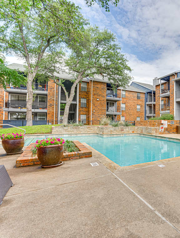 A pool surrounded by a brick building and trees.