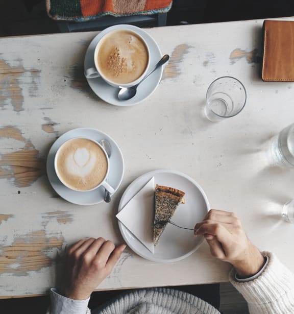 two people sitting at a table with coffee and a piece of cake